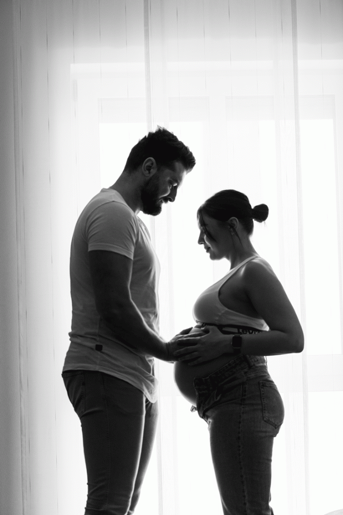 Schwangere Frau und Mann stehen sich gegenüber und halten den Babybauch.