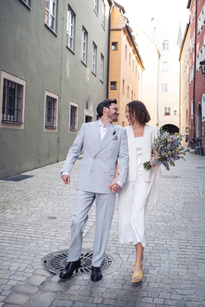 Brautpaar in Regensburgs Altstadt, Braut und Bräutigam halten sich an den Händen und gehen in Altstadtgasse entlang
